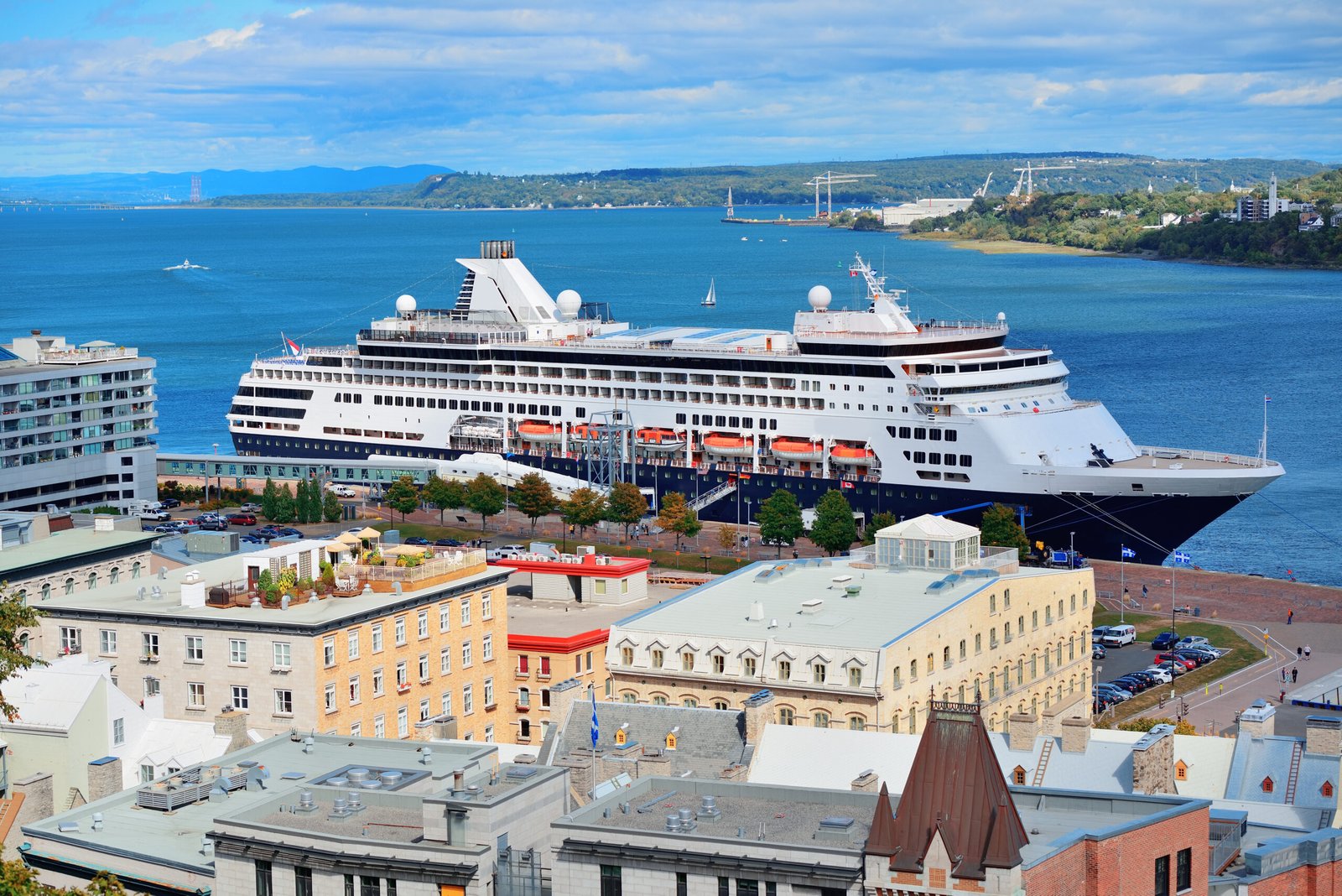 Cruise ship in river in Quebec City with blue sky and historical buildings.